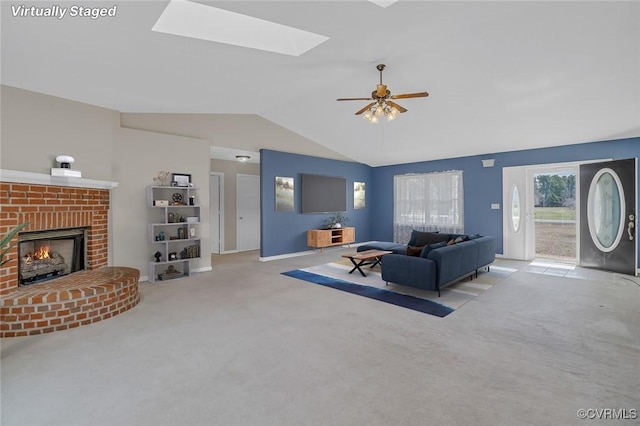 living area with lofted ceiling with skylight, carpet flooring, baseboards, a brick fireplace, and ceiling fan