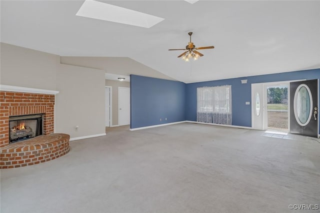 unfurnished living room featuring lofted ceiling with skylight, a ceiling fan, carpet flooring, a fireplace, and baseboards