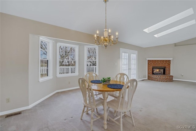 dining room featuring visible vents, baseboards, carpet flooring, vaulted ceiling with skylight, and a fireplace