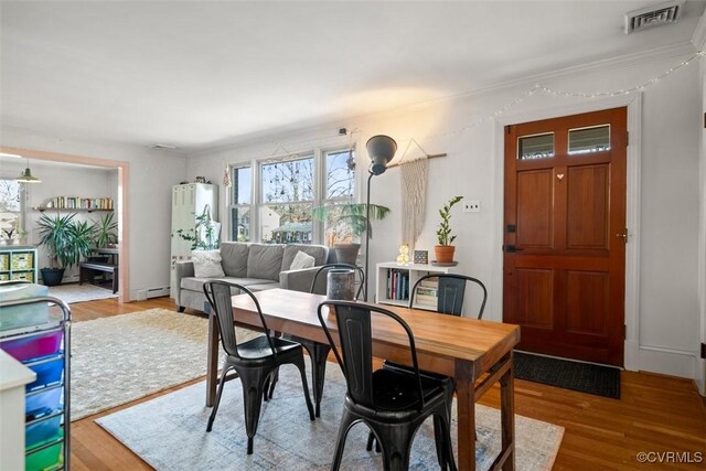 dining room featuring wood finished floors, visible vents, and a baseboard radiator