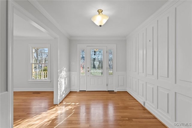 entrance foyer with a decorative wall, a wainscoted wall, light wood-type flooring, and ornamental molding