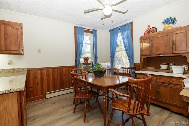 dining area with light wood-style floors, a baseboard radiator, wooden walls, and wainscoting