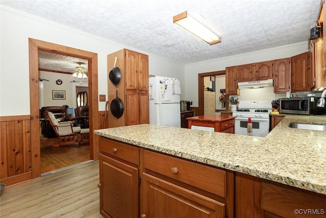 kitchen featuring light wood finished floors, ornamental molding, wainscoting, white appliances, and under cabinet range hood