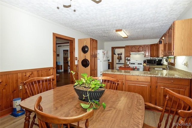 dining room with ceiling fan, light wood-type flooring, wood walls, and wainscoting