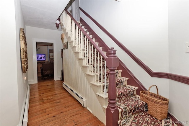 stairway featuring a baseboard heating unit, baseboard heating, and wood finished floors