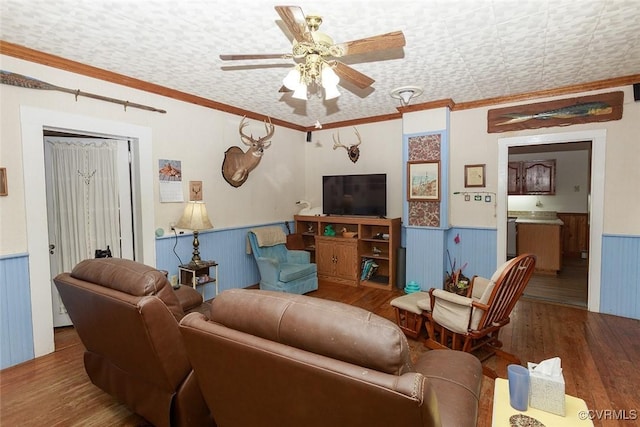 living room with ornamental molding, wainscoting, wood finished floors, and a ceiling fan