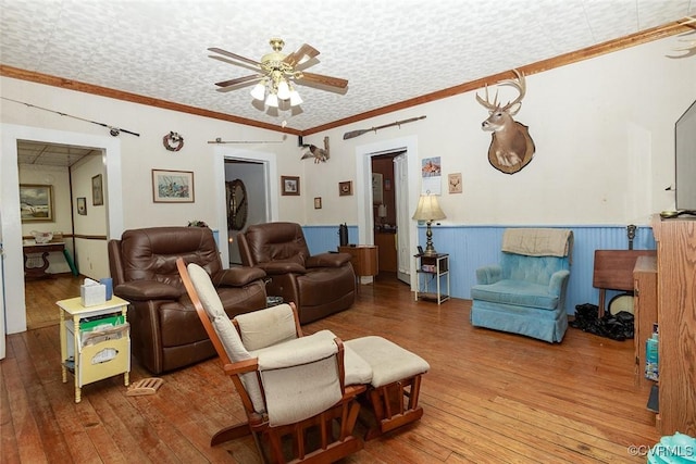 living area featuring hardwood / wood-style flooring, crown molding, a ceiling fan, and a wainscoted wall