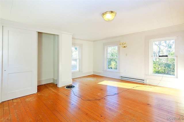 empty room featuring a baseboard heating unit, hardwood / wood-style flooring, and a healthy amount of sunlight