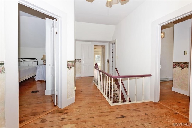 hall featuring lofted ceiling, a baseboard heating unit, hardwood / wood-style flooring, and an upstairs landing