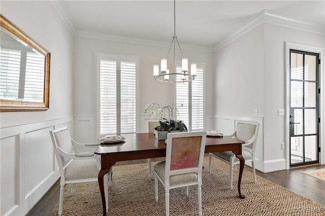 dining room featuring a wainscoted wall, crown molding, a decorative wall, an inviting chandelier, and dark wood-type flooring