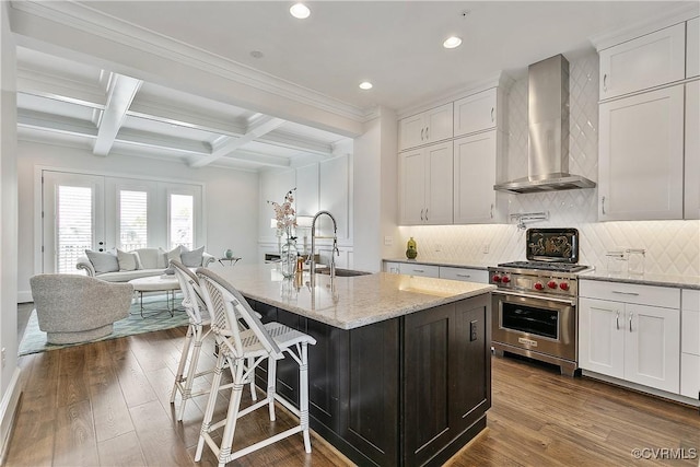 kitchen featuring designer stove, open floor plan, a kitchen island with sink, wall chimney range hood, and white cabinetry