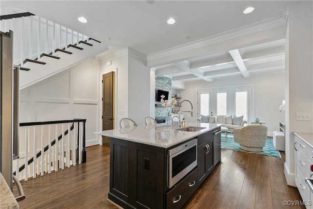 kitchen with a kitchen island with sink, stainless steel appliances, coffered ceiling, a sink, and dark wood finished floors