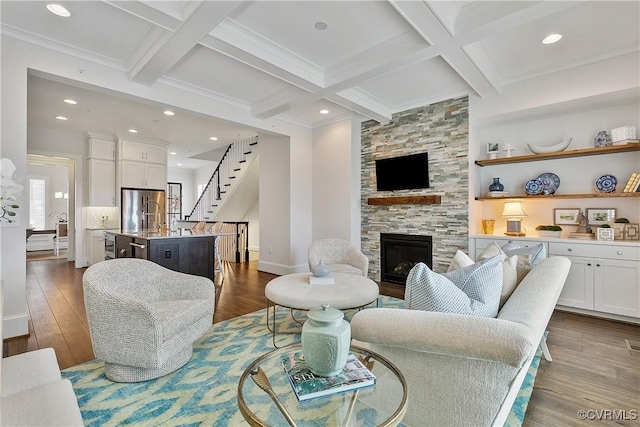 living room featuring a large fireplace, beam ceiling, stairway, and wood finished floors