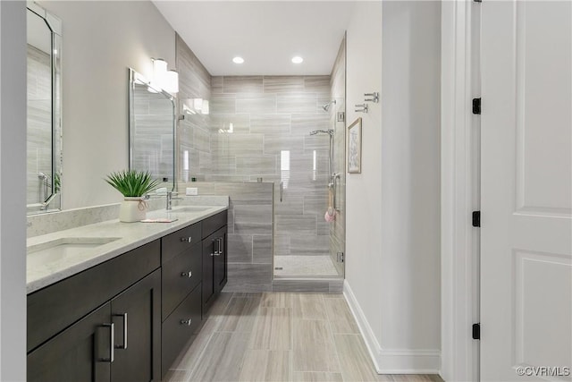 bathroom with a stall shower, a sink, baseboards, and double vanity