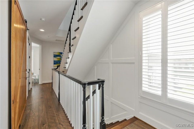 hall with recessed lighting, dark wood finished floors, an upstairs landing, and a decorative wall