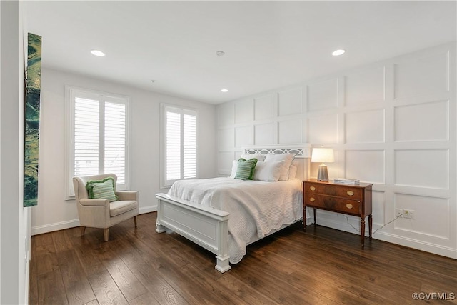 bedroom with baseboards, a decorative wall, dark wood-style flooring, and recessed lighting