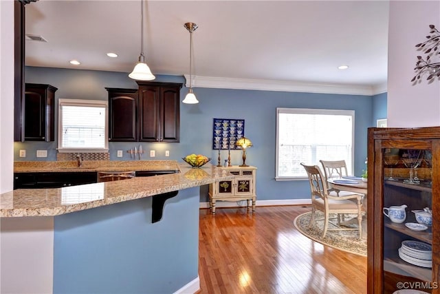 kitchen featuring baseboards, light wood-style flooring, ornamental molding, hanging light fixtures, and a kitchen bar