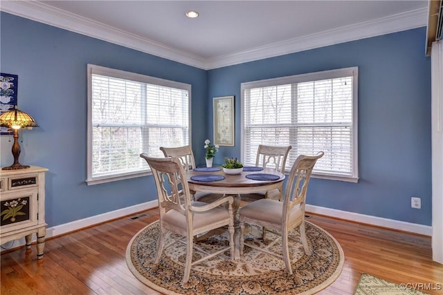 dining space with baseboards, wood finished floors, visible vents, and crown molding