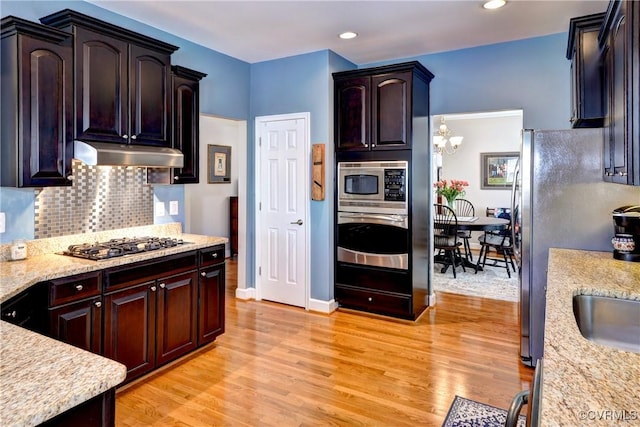 kitchen featuring tasteful backsplash, under cabinet range hood, light wood-style flooring, and stainless steel appliances