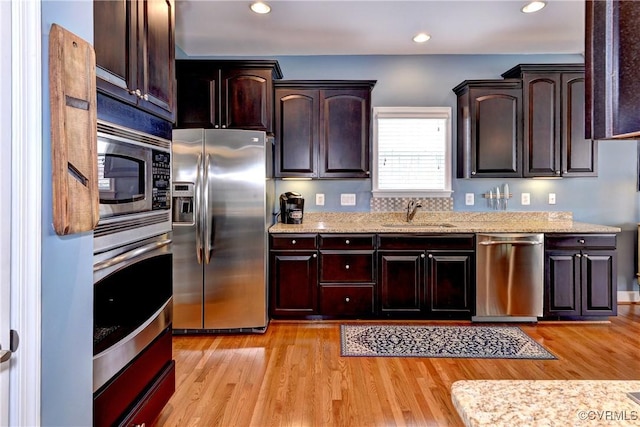 kitchen with appliances with stainless steel finishes, light wood-type flooring, a sink, and light stone countertops