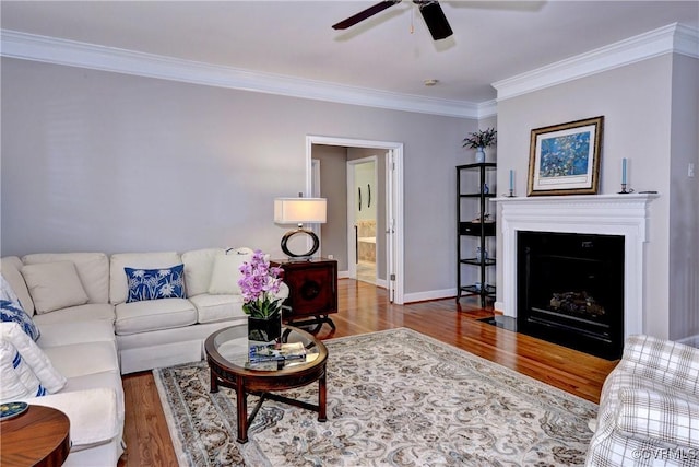 living area with baseboards, a fireplace with flush hearth, wood finished floors, and crown molding