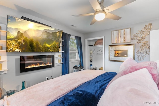 bedroom with a closet, visible vents, a ceiling fan, and a glass covered fireplace