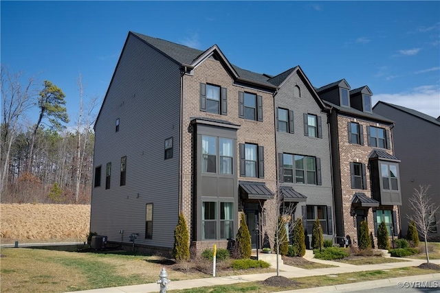 townhome / multi-family property with a front lawn, central AC, and brick siding