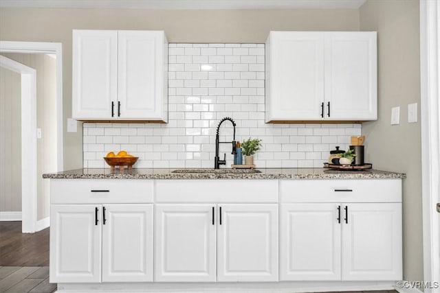 kitchen with light stone counters, white cabinetry, a sink, and tasteful backsplash