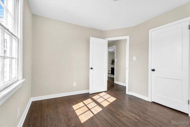 unfurnished bedroom with baseboards and dark wood-type flooring