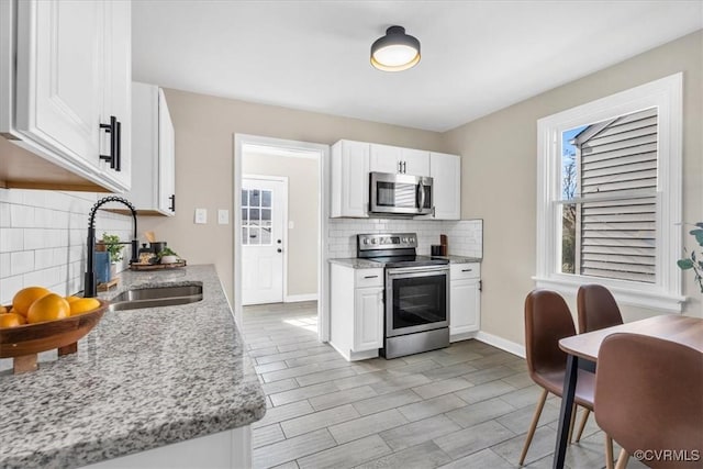 kitchen with white cabinets, light stone countertops, stainless steel appliances, and a sink