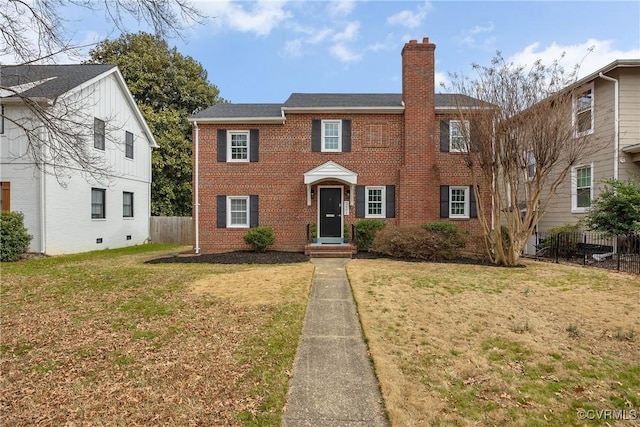 colonial inspired home with brick siding, fence, a chimney, and a front lawn