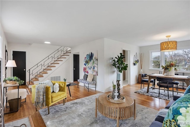 living room featuring light wood-style flooring, stairs, visible vents, and baseboards