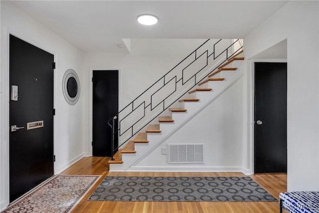 entrance foyer with stairway, wood finished floors, visible vents, and baseboards