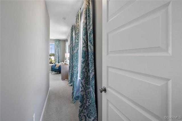 hallway featuring light carpet and baseboards