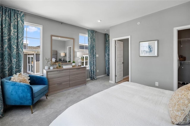 bedroom featuring a walk in closet, a closet, light colored carpet, and multiple windows