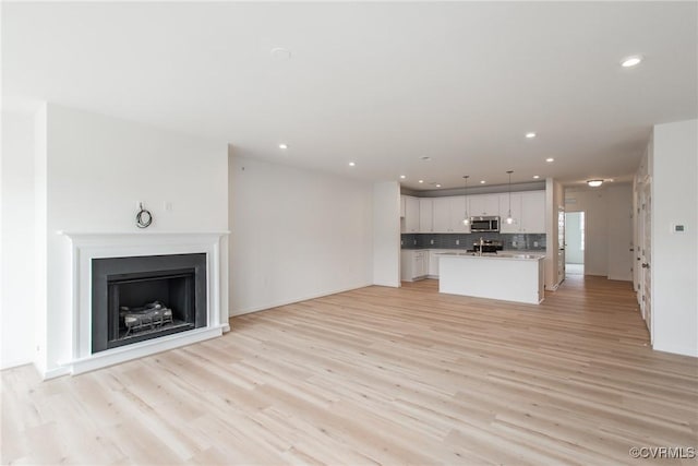 unfurnished living room featuring recessed lighting, a sink, a fireplace, and light wood finished floors