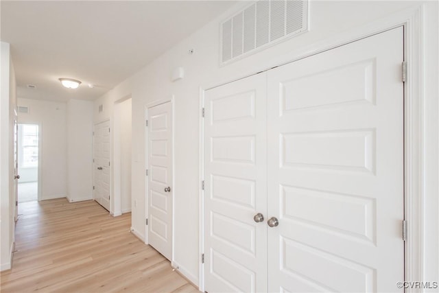 corridor with light wood-type flooring, visible vents, and baseboards