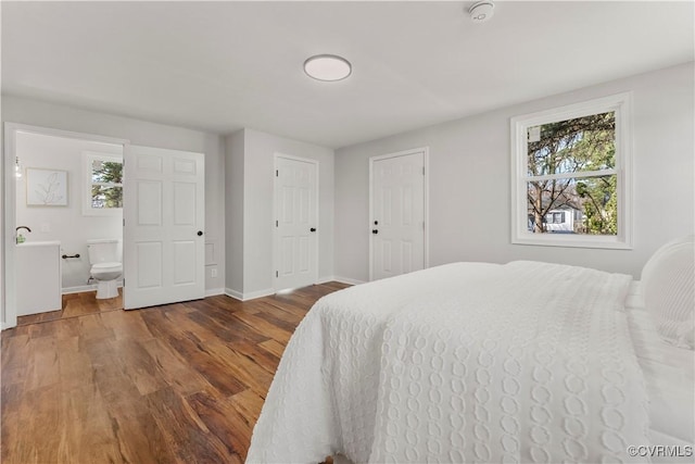 bedroom with ensuite bathroom, baseboards, and wood finished floors