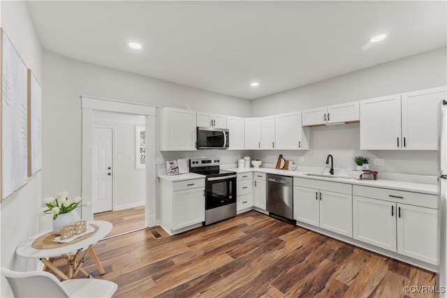 kitchen with a sink, wood finished floors, white cabinets, light countertops, and appliances with stainless steel finishes