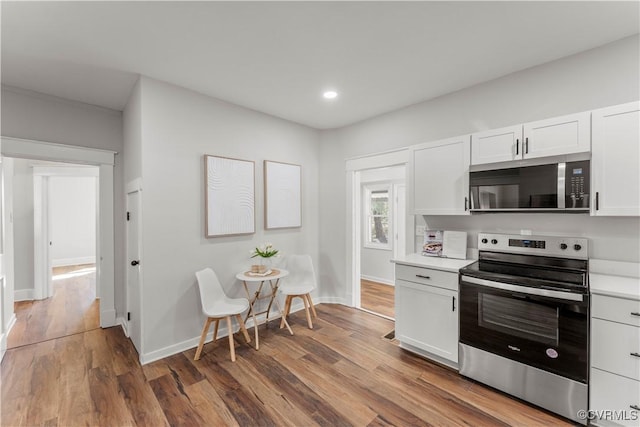 kitchen featuring stainless steel appliances, wood finished floors, light countertops, and white cabinetry