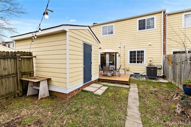 back of property with a deck, an outbuilding, a fenced backyard, central air condition unit, and a storage shed