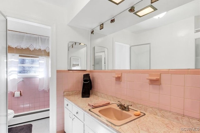 bathroom with wainscoting, toilet, vanity, a baseboard heating unit, and tile walls