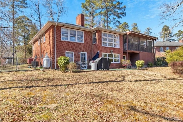 rear view of house featuring brick siding, a chimney, a lawn, a sunroom, and fence