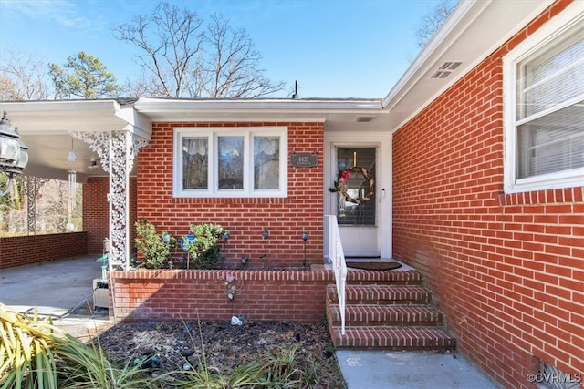 view of exterior entry with brick siding and an attached carport