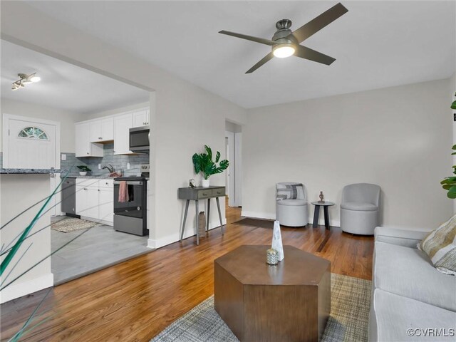 living room with light wood-type flooring, a ceiling fan, and baseboards