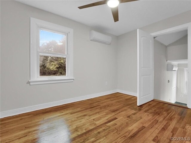 unfurnished room with lofted ceiling, a ceiling fan, light wood-type flooring, a wall mounted air conditioner, and baseboards