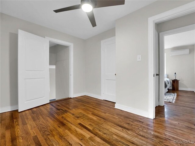 unfurnished bedroom featuring an AC wall unit, wood finished floors, a ceiling fan, and baseboards