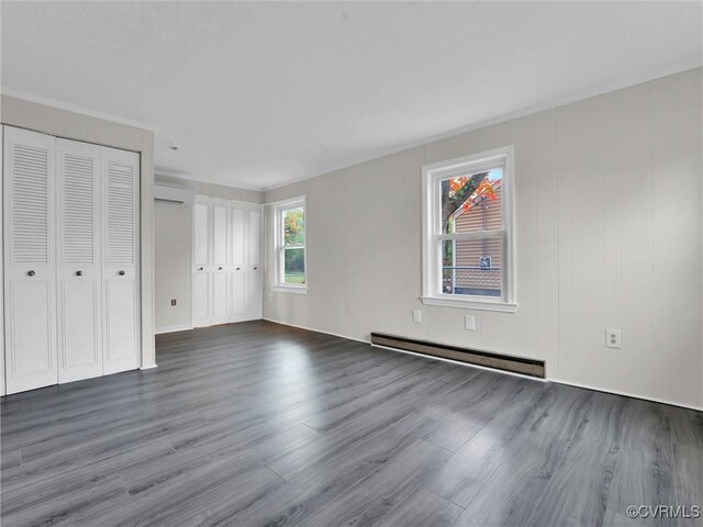 unfurnished bedroom with multiple closets, a baseboard radiator, wood finished floors, and a wall mounted air conditioner