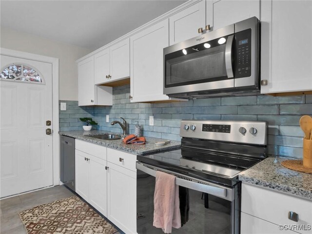 kitchen with decorative backsplash, white cabinets, light stone counters, appliances with stainless steel finishes, and a sink