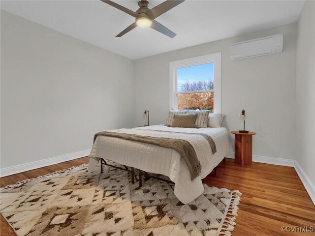 bedroom featuring baseboards, an AC wall unit, and wood finished floors